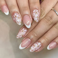 Short glossy almond-shaped false nails with French manicure style, white powder flowers, and glitter accents.