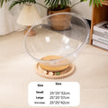 Transparent acrylic cat space capsule bed with a turntable base on a wooden floor.