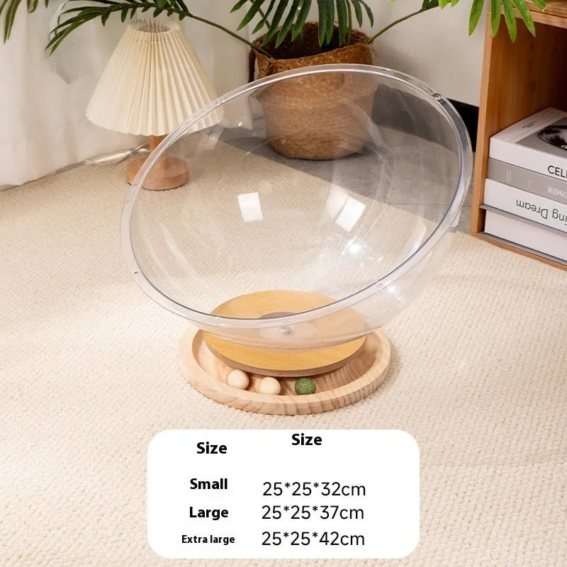 Transparent acrylic cat space capsule bed with a turntable base on a wooden floor.