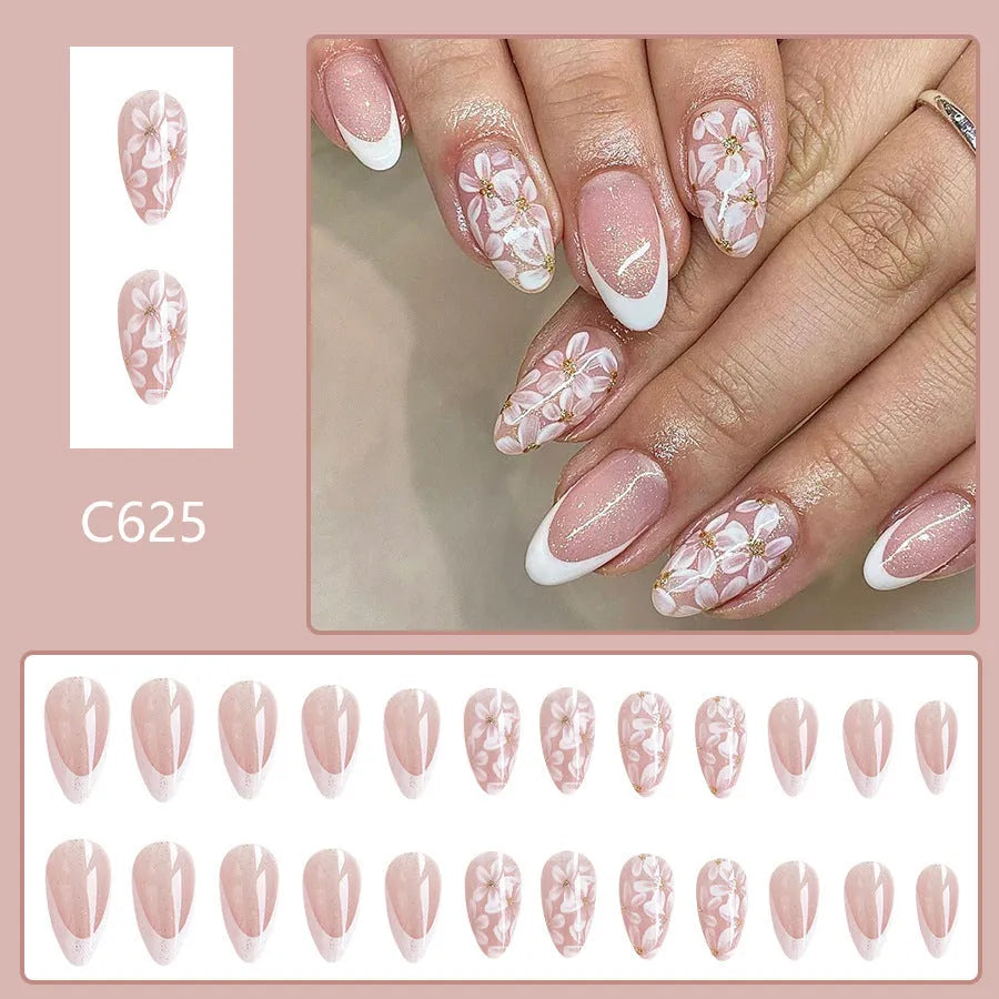 Short glossy almond-shaped false nails with French manicure style, white powder flowers, and glitter accents.