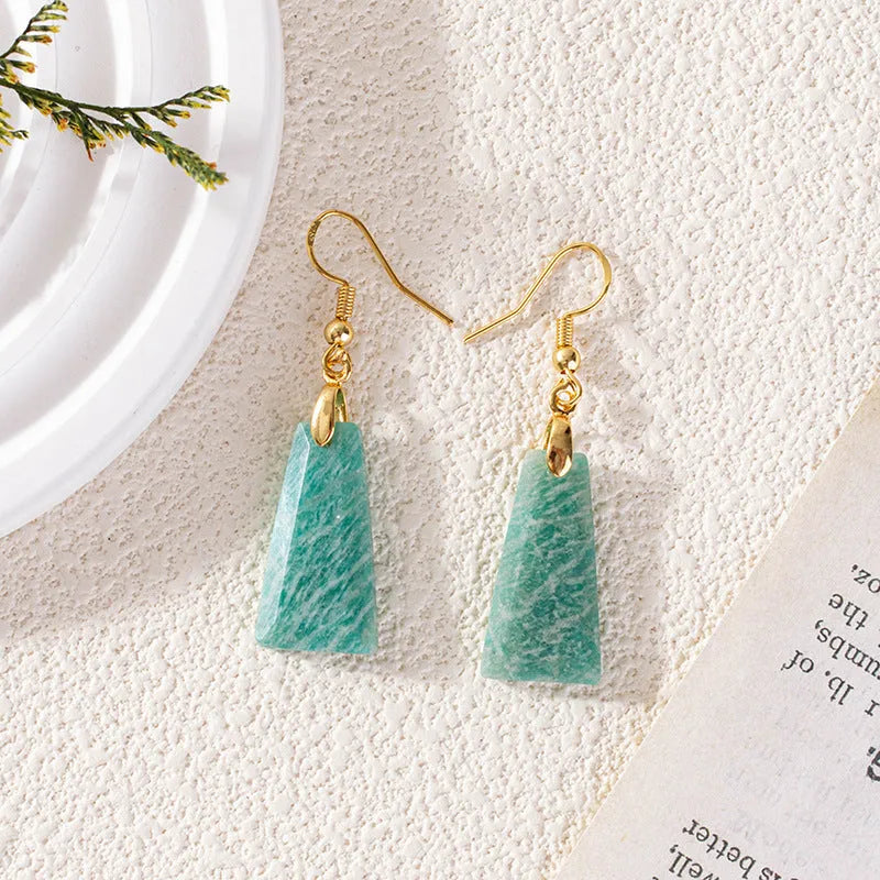 Gold trapezoid earrings with rough-cut amazonite stone and geometric detail on white background.