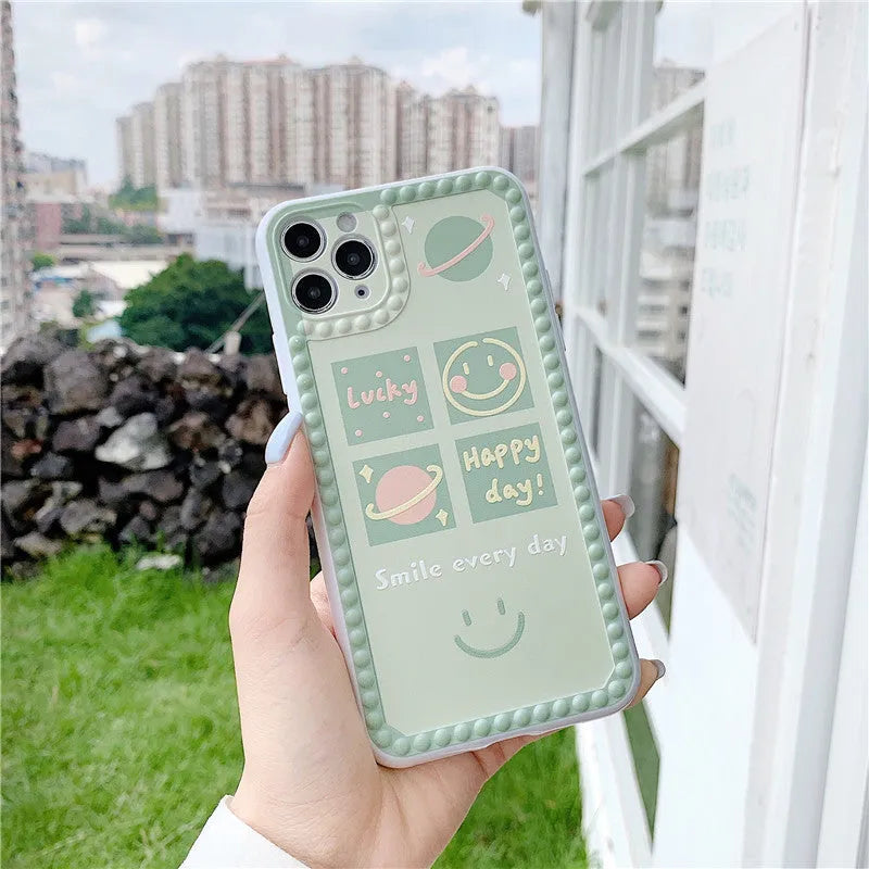 Green iPhone case with geometric smiley face pattern and polka dot border on a table.