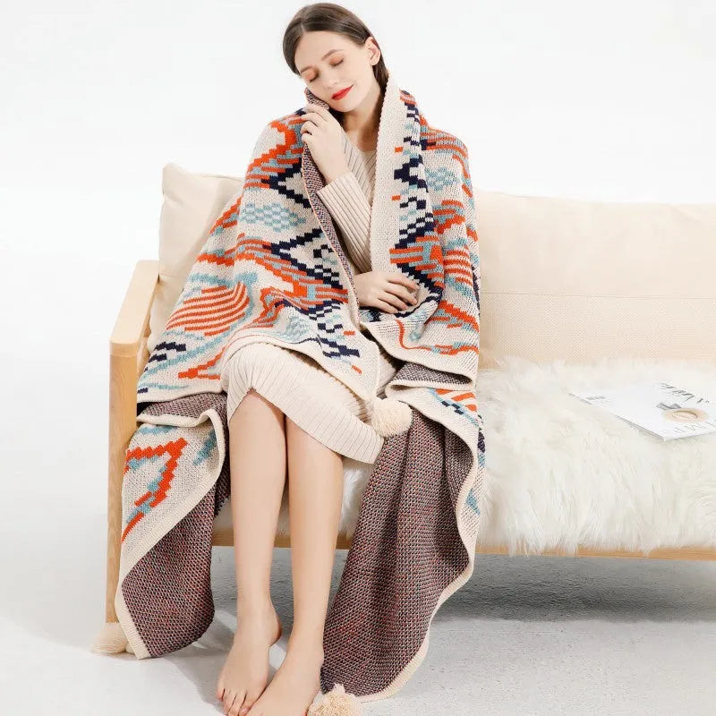 Bohemian style acrylic sofa blanket with tassel fringe in a geometric blue and pink pattern.