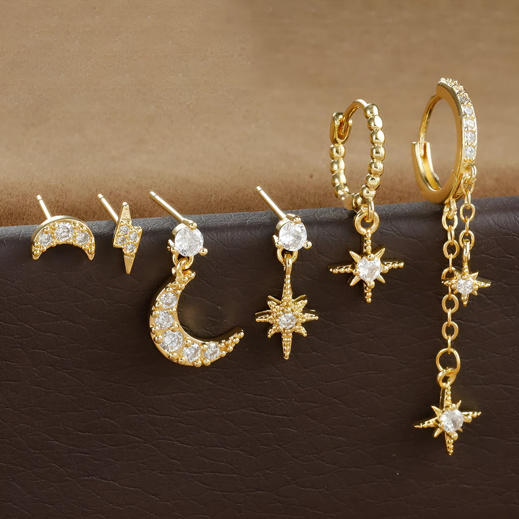 Set of six gold electroplated earrings with zircon studs and chain tassels on a flat surface.