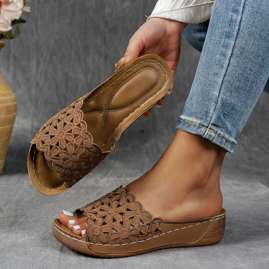Women's black wedge beach slippers with flower cutout design on the PVC upper and a rubber sole.