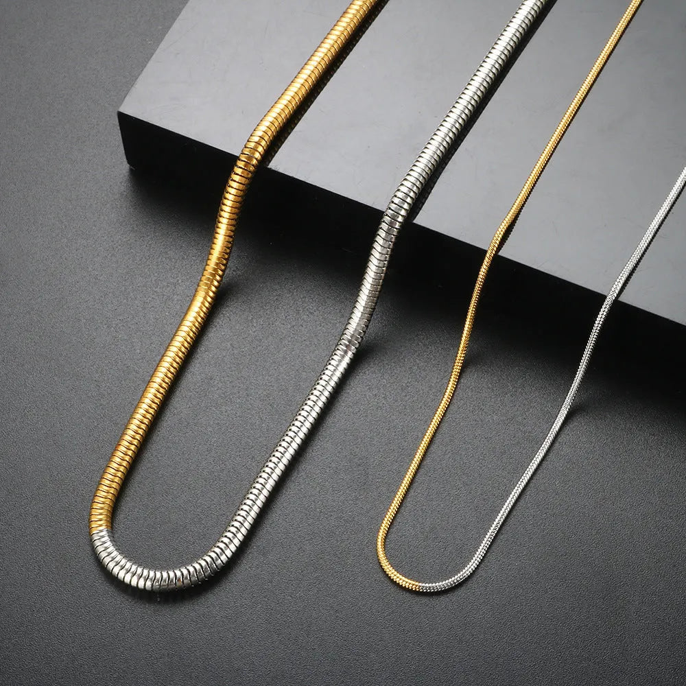Close-up of a 3mm wide golden snake bone chain necklace with a geometric design on a dark background.