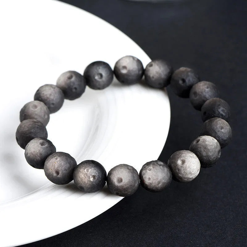 Close-up of a natural obsidian crater ball bracelet with grinding-treated beads on a wrist.