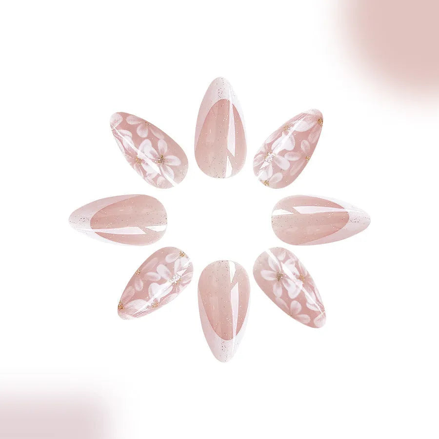 Short glossy almond-shaped false nails with French manicure style, white powder flowers, and glitter accents.