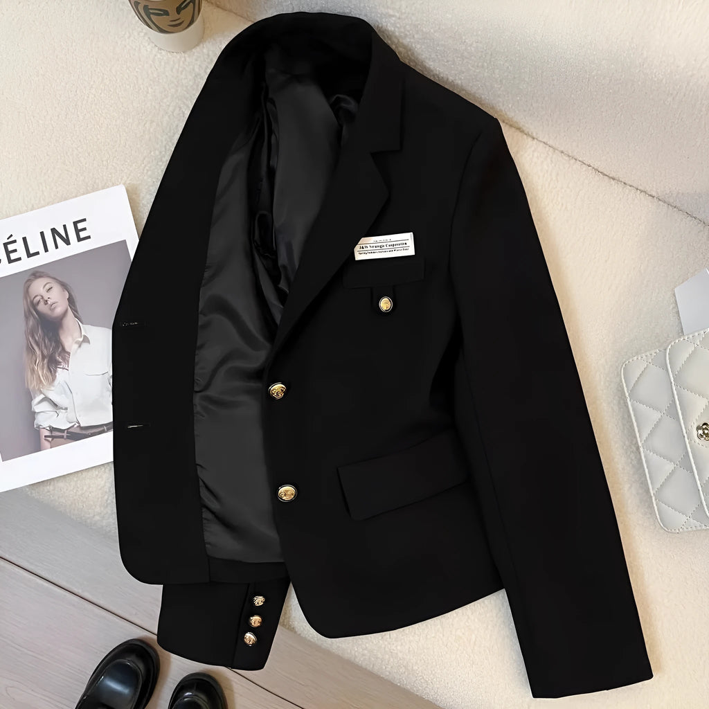 A woman wearing a black, loose-fit, short polyester suit coat with long sleeves and pockets.