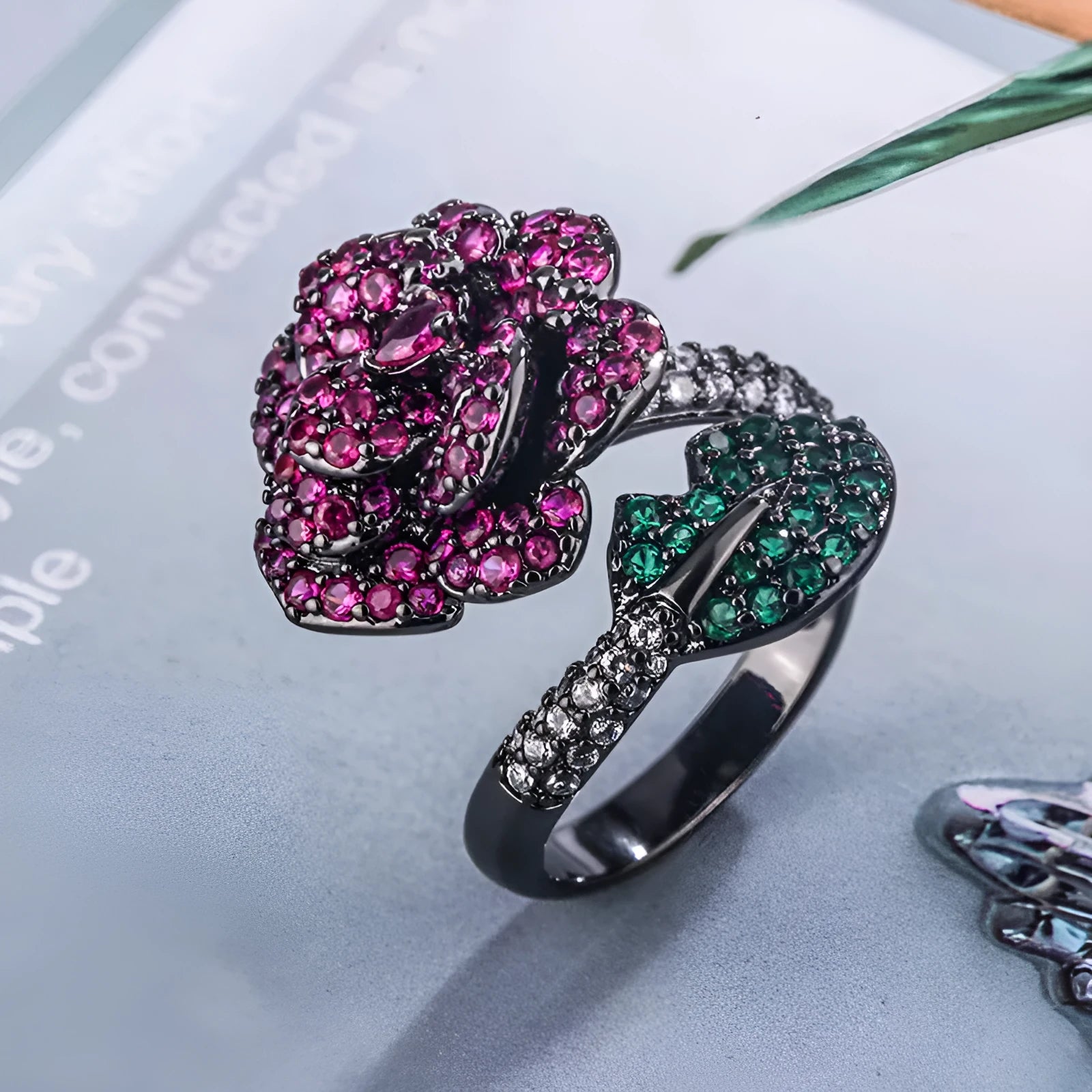 A black gold geometric flower ring with simulated red corundum stones on a model's hand.