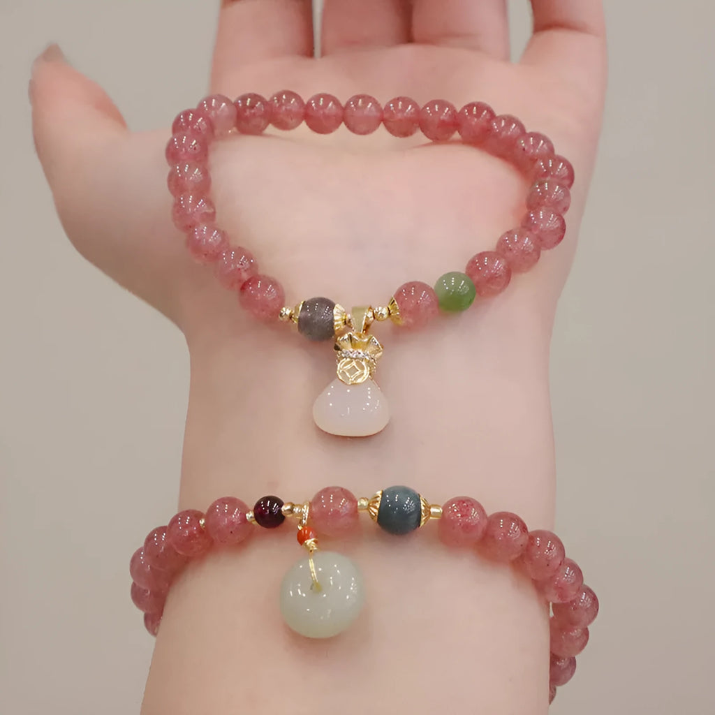 Close-up of a women's strawberry quartz bead bracelet with a geometric pattern and a central gold-tone purse charm.
