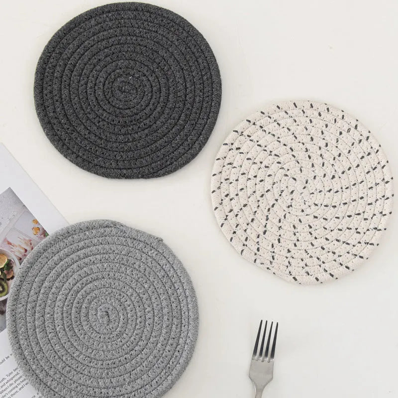 Three round grey cotton cord coasters arranged on a wooden table.