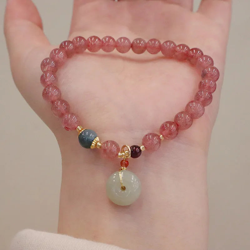 Close-up of a women's strawberry quartz bead bracelet with a geometric pattern and a central gold-tone purse charm.