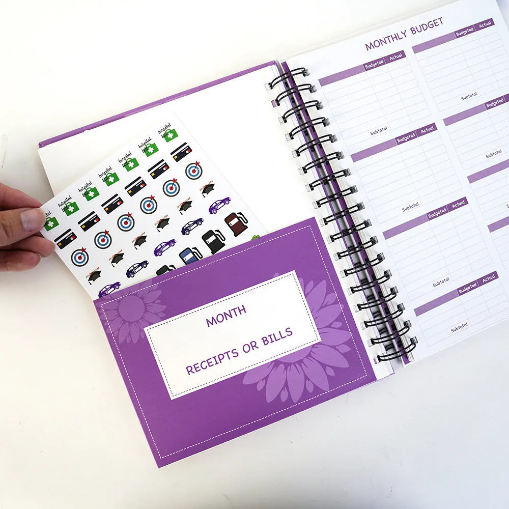 Purple coil-bound financial planning notebook with pen and stickers on a desk.
