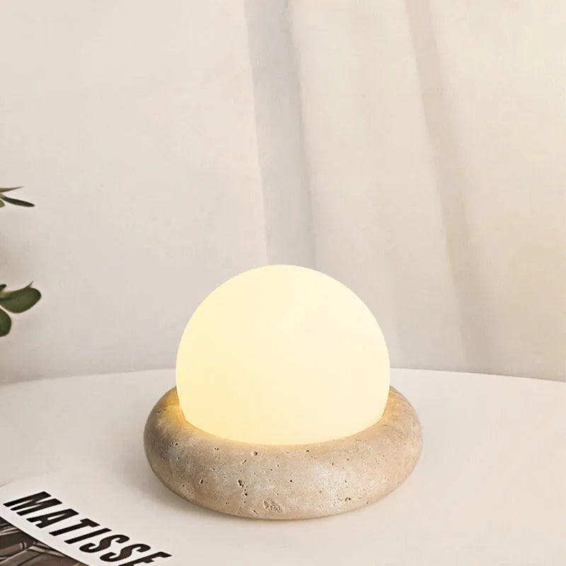 Cream-coloured modern bedside lamp with remote control on a table.
