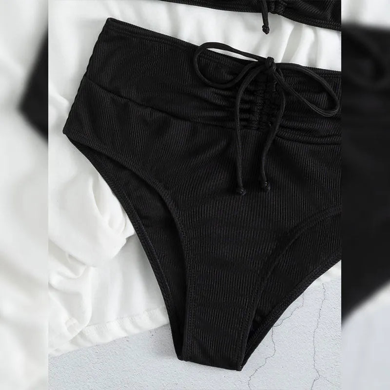 Black women's bikini swimsuit with sling top and high-waisted shorts on a white background