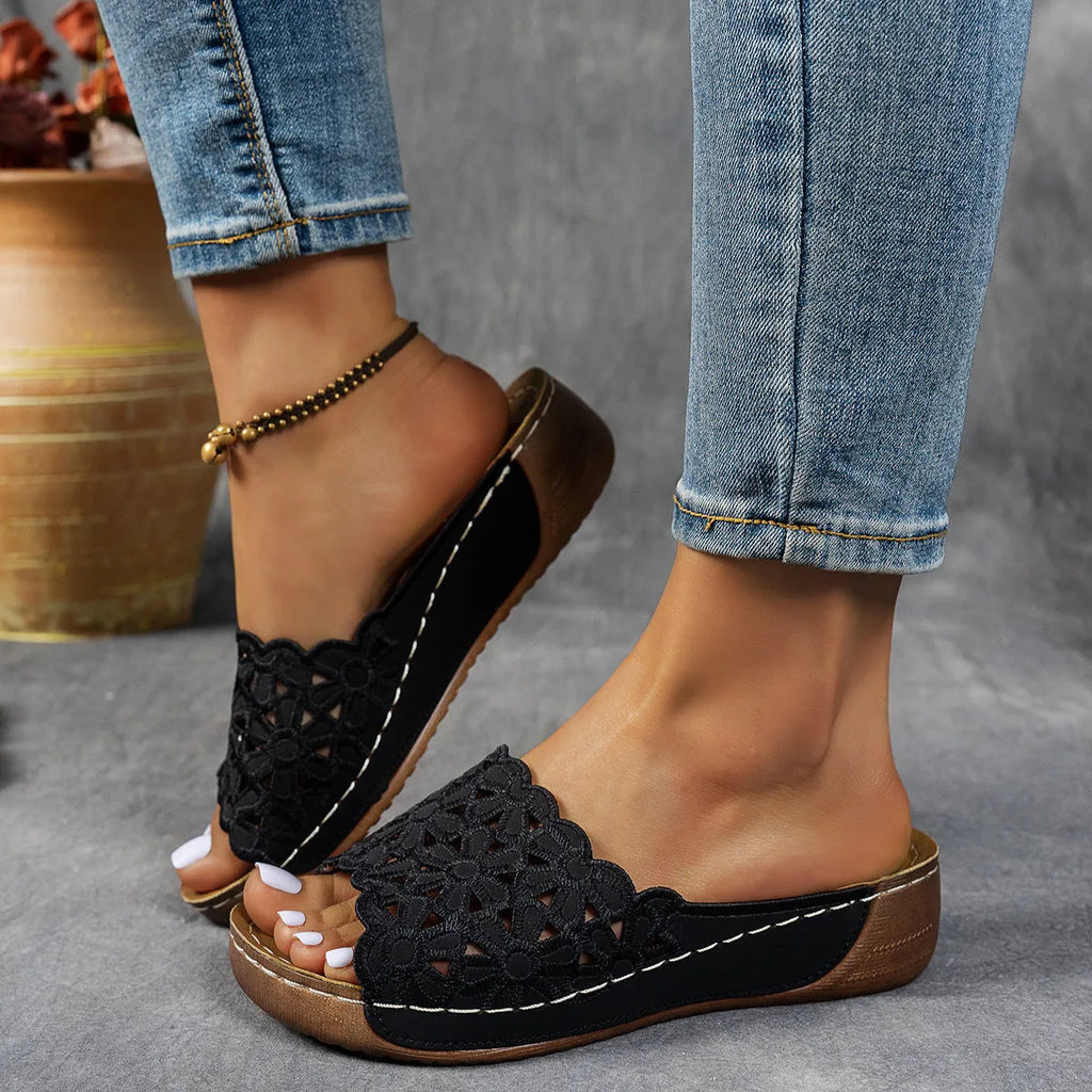 Women's black wedge beach slippers with flower cutout design on the PVC upper and a rubber sole.