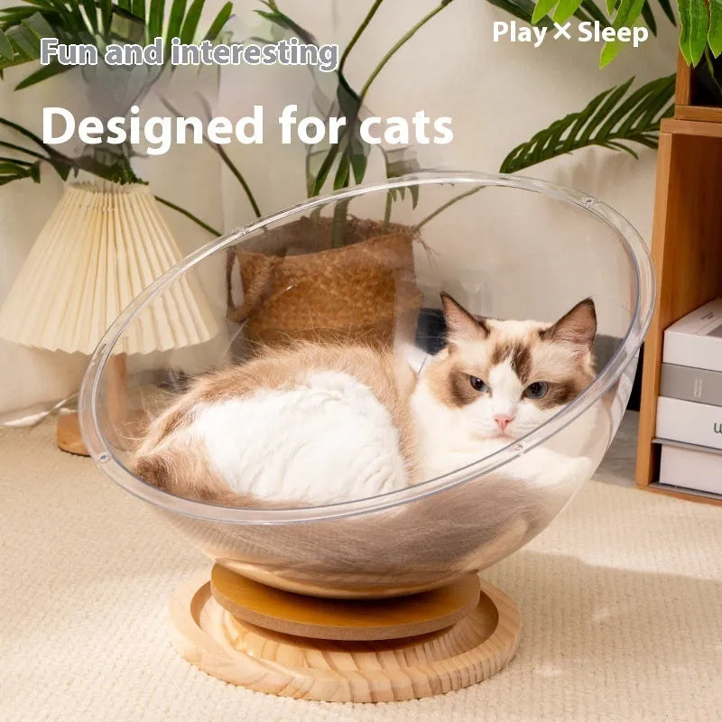 Transparent acrylic cat space capsule bed with a turntable base on a wooden floor.