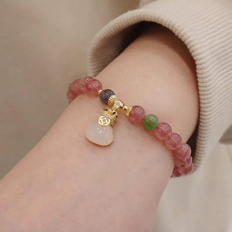 Close-up of a women's strawberry quartz bead bracelet with a geometric pattern and a central gold-tone purse charm.