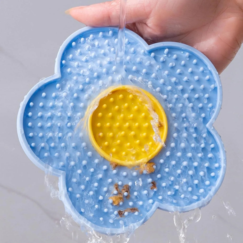 Flower-shaped silicone dog lick mat in pink with suction cups on the underside, shown on a tiled floor.