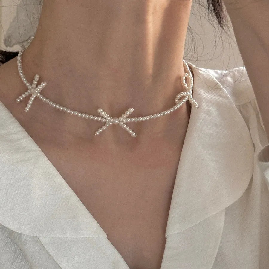 White bow-shaped imitation pearl necklace with an adjustable chain on a woman's clavicle.