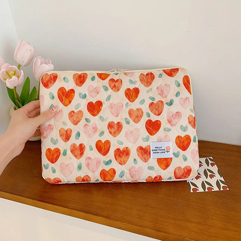 Printed cloth laptop bag showing floral and heart patterns in green, pink, and red colourways
