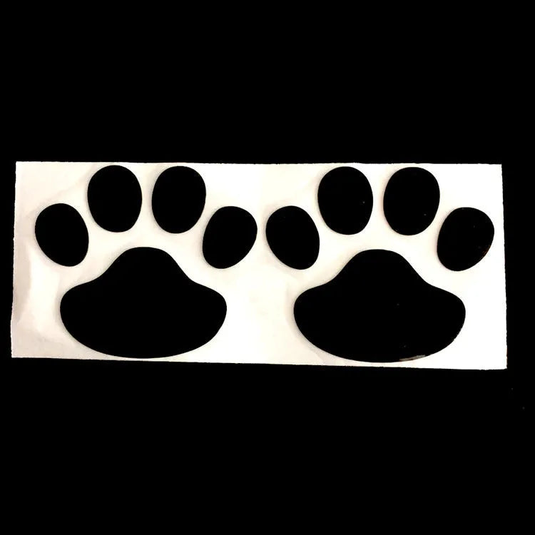 Close-up of a black PVC car sticker with dog footprints and a hand-shaped brush texture on a car bumper.