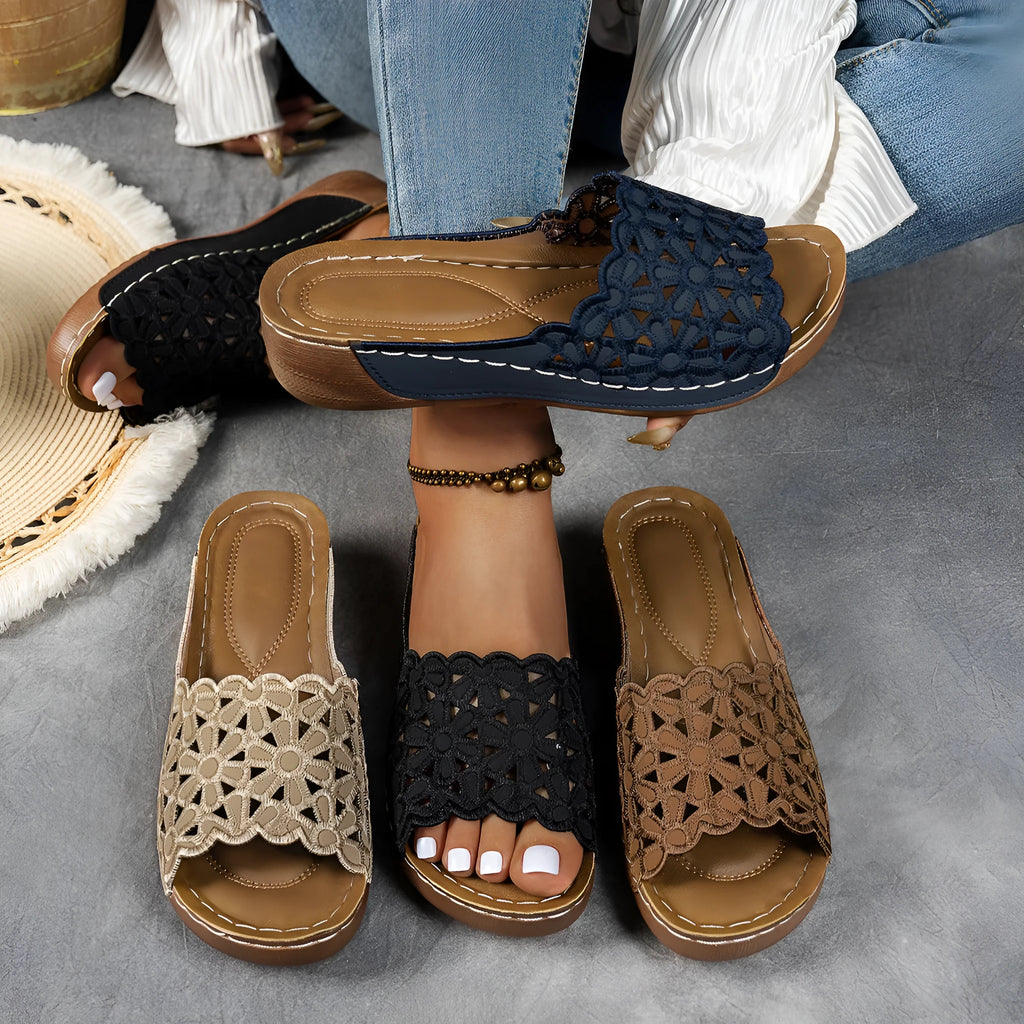 Women's black wedge beach slippers with flower cutout design on the PVC upper and a rubber sole.