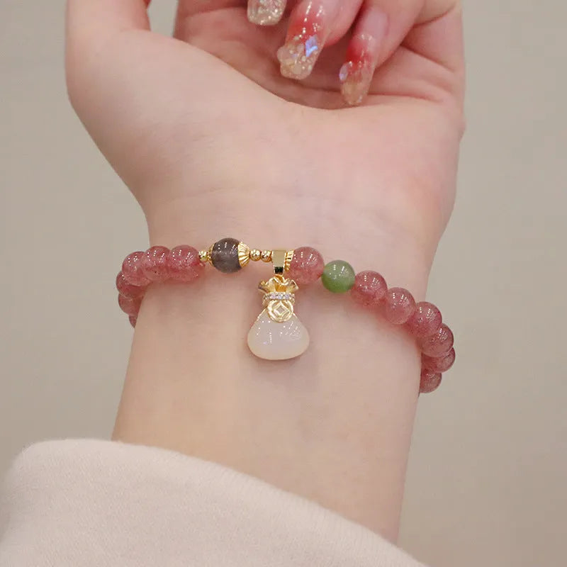 Close-up of a women's strawberry quartz bead bracelet with a geometric pattern and a central gold-tone purse charm.