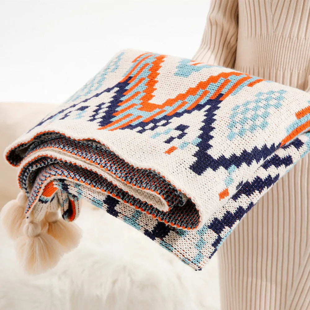 Bohemian style acrylic sofa blanket with tassel fringe in a geometric blue and pink pattern.