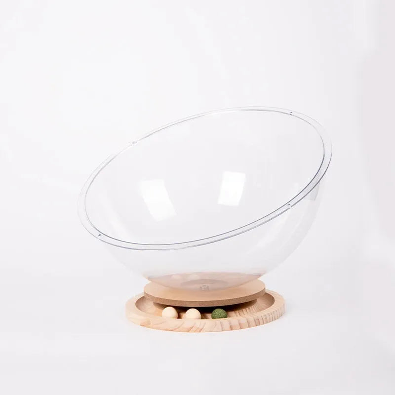 Transparent acrylic cat space capsule bed with a turntable base on a wooden floor.
