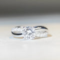Geometric twisted silver-coloured band moissanite ring with a 1 carat stone in a four-claw setting.