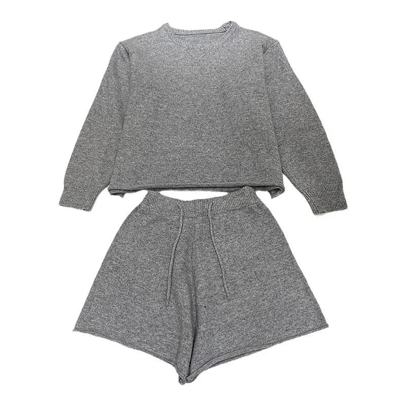 Woman wearing a loose grey long sleeve sweater and matching wide leg knit shorts lounge set.