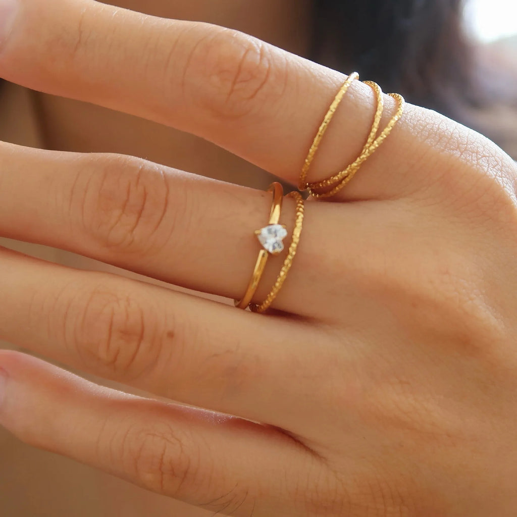 A golden stainless steel ring showing both the love heart design and the oval design option on a hand.