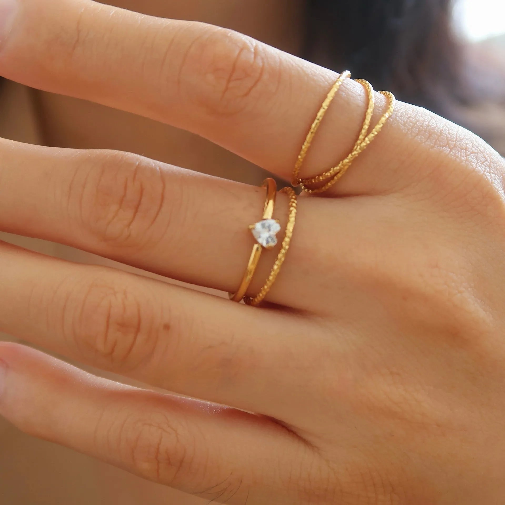 A golden stainless steel ring showing both the love heart design and the oval design option on a hand.
