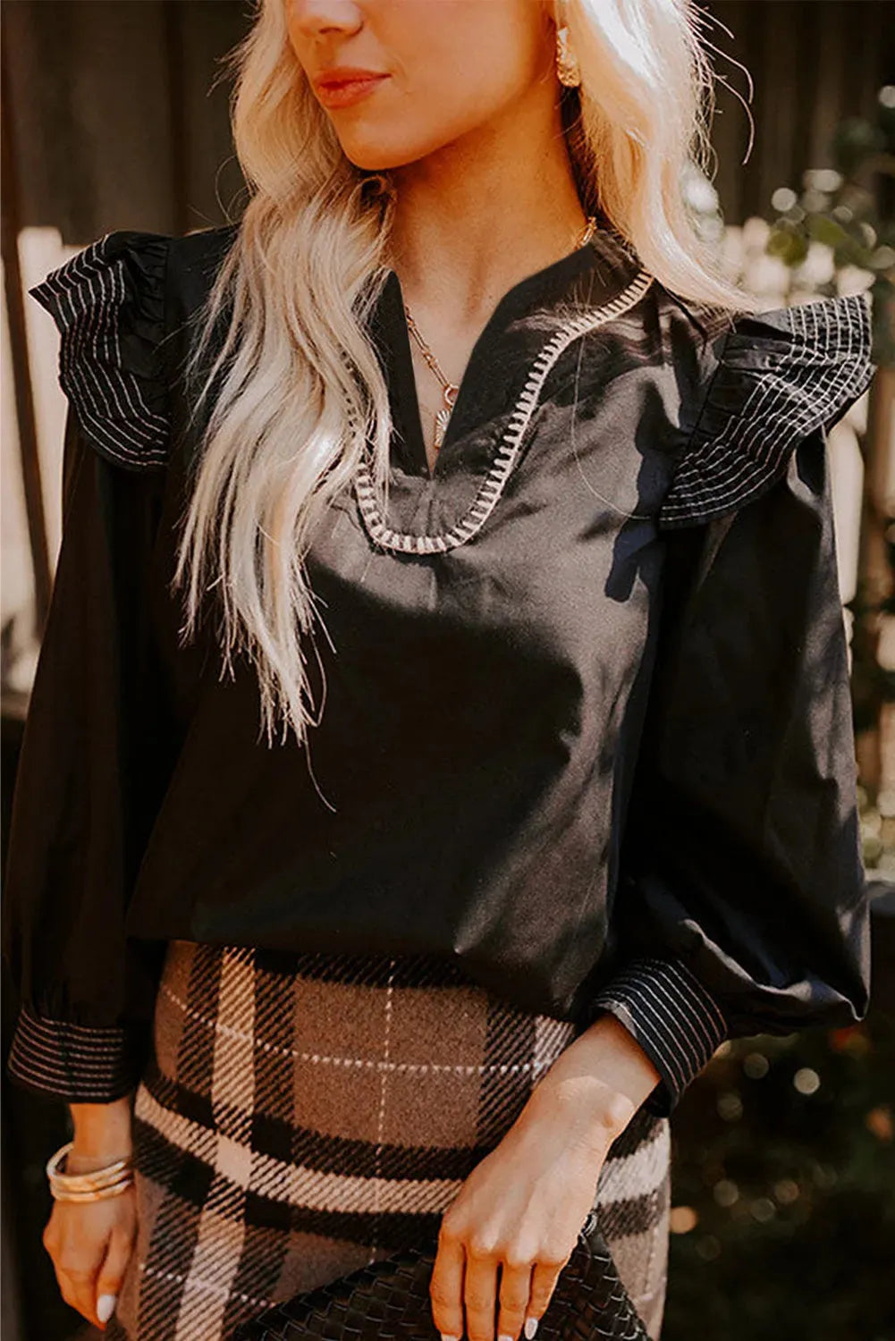 Black women's v-neck blouse with long ruffle sleeves and contrast stitching.