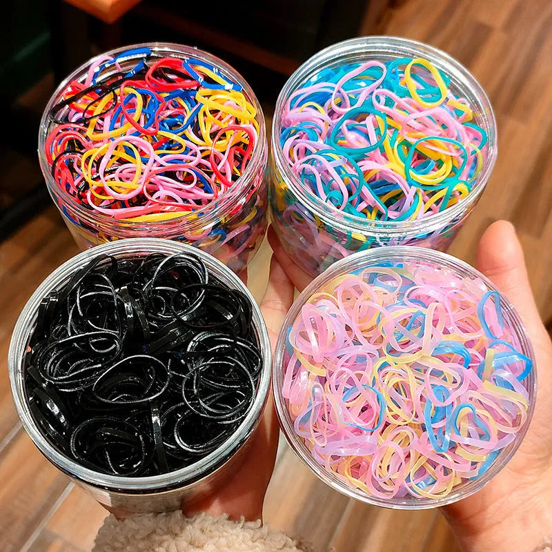 Multi-colour assortment of small TPU elastic baby hair ties in a clear reusable storage container.