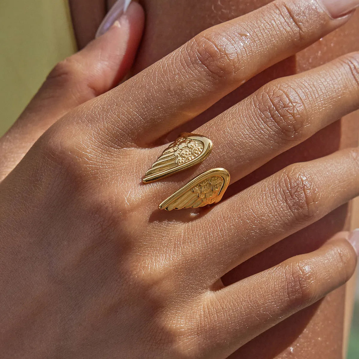 Adjustable stainless steel ring with wing design in an electroplated colour on a hand.