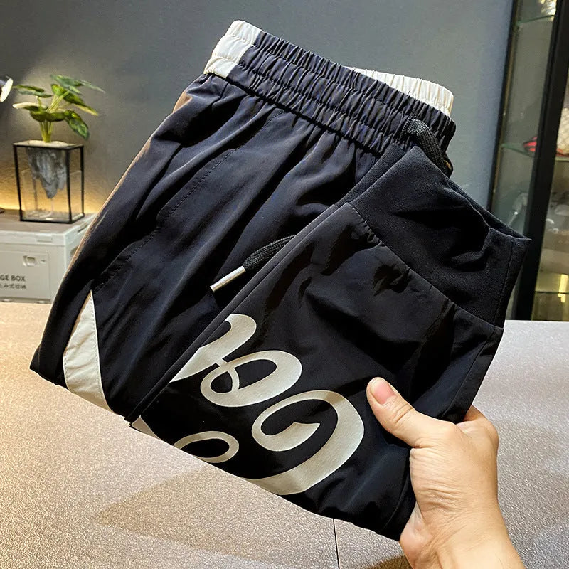 Black cotton men's cropped casual trousers with a banded ankle cuff laid flat.