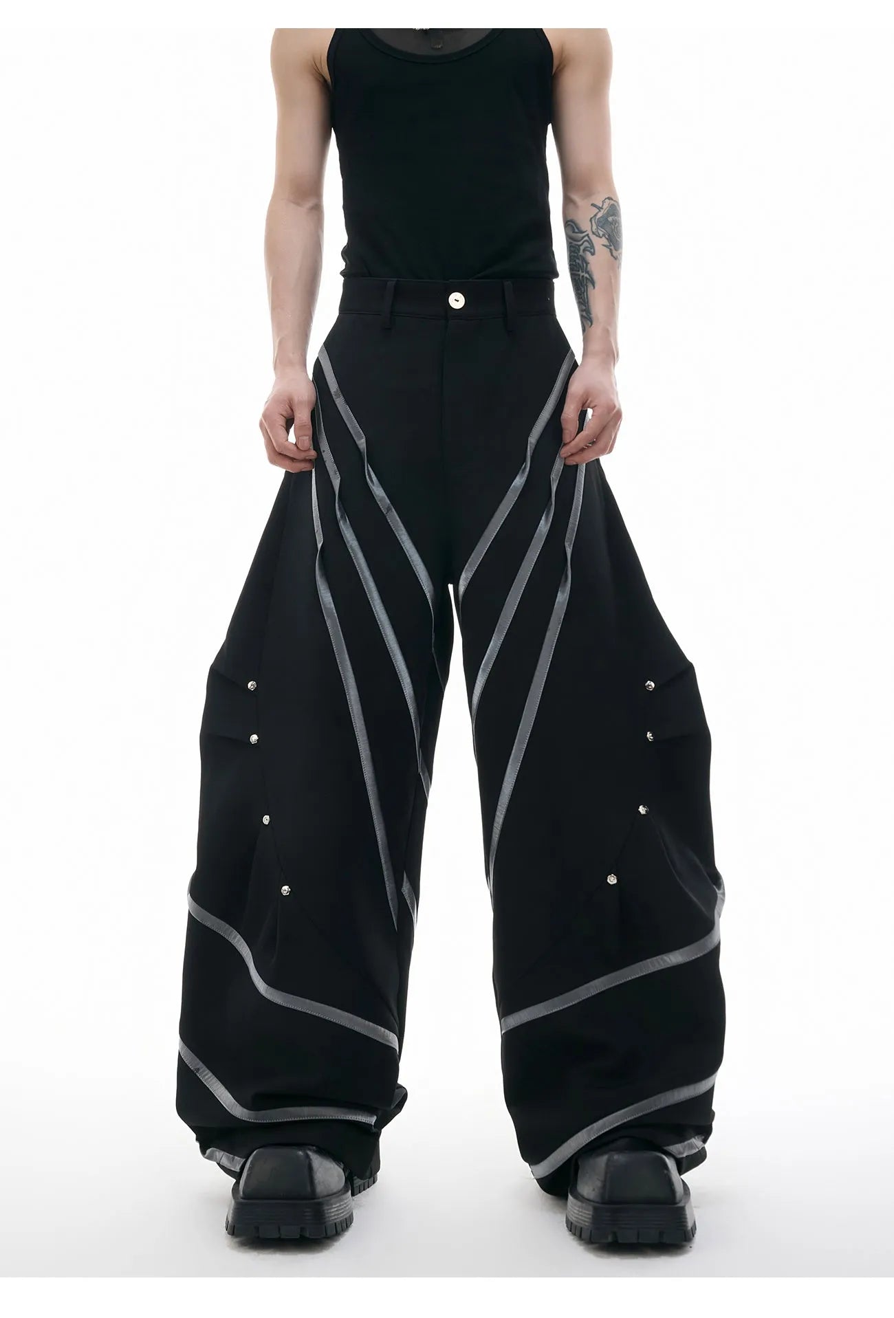 Men's black polyester trousers with metal striped rivets and pleated detail on a white background.