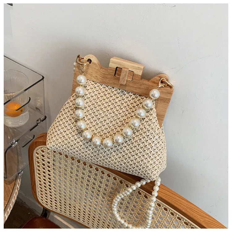 Women's woven straw shoulder bag with pearl chain detail in beige, showing horizontal square shape and single strap.