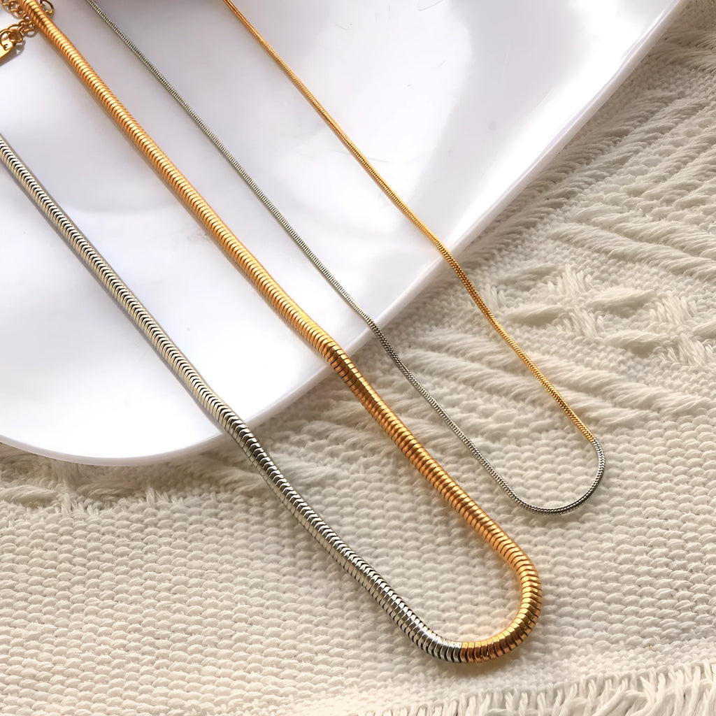 Close-up of a 3mm wide golden snake bone chain necklace with a geometric design on a dark background.