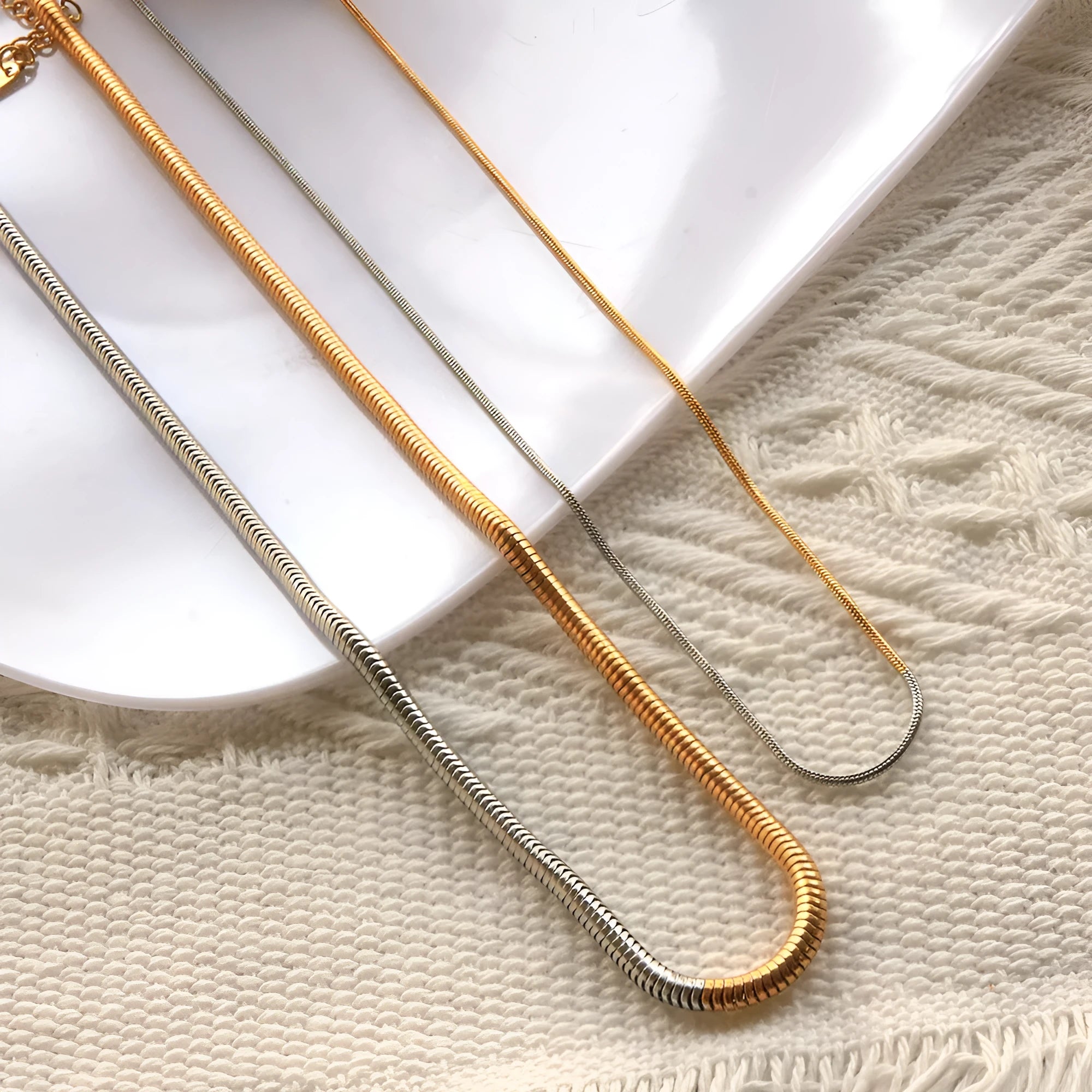 Close-up of a 3mm wide golden snake bone chain necklace with a geometric design on a dark background.
