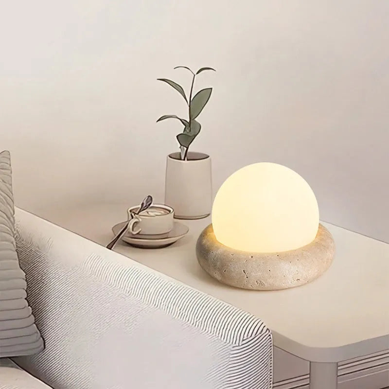 Cream-coloured modern bedside lamp with remote control on a table.
