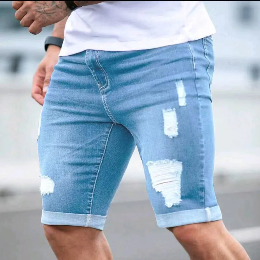 Sky blue men's denim shorts with manual distressing holes on the legs, showing a low waist and zip fly.