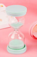 Handcrafted glass sand clock timer on a desk, showing blue sand, with modern simplicity design.