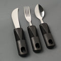 Stainless steel adaptive knife, fork, and spoon set with black rubberised easy-grip handles.
