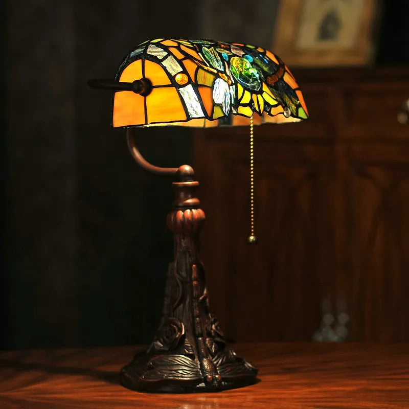 Tiffany table lamp with coloured stained glass shade and resin base on wooden desk
