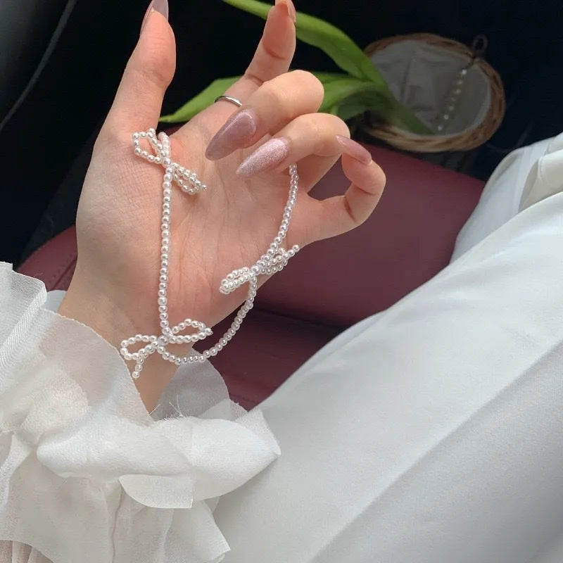 White bow-shaped imitation pearl necklace with an adjustable chain on a woman's clavicle.