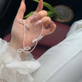 White bow-shaped imitation pearl necklace with an adjustable chain on a woman's clavicle.